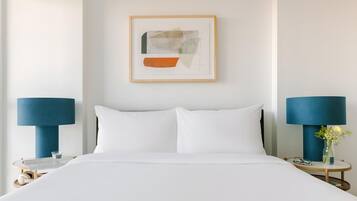 Habitación de hotel con cama, dos mesitas de noche con lámparas, una obra de arte abstracta enmarcada en la pared y un jarrón con flores sobre una de las mesitas.