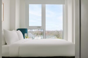 Een moderne slaapkamer met een groot raam, een bed en een blauwe stoel.