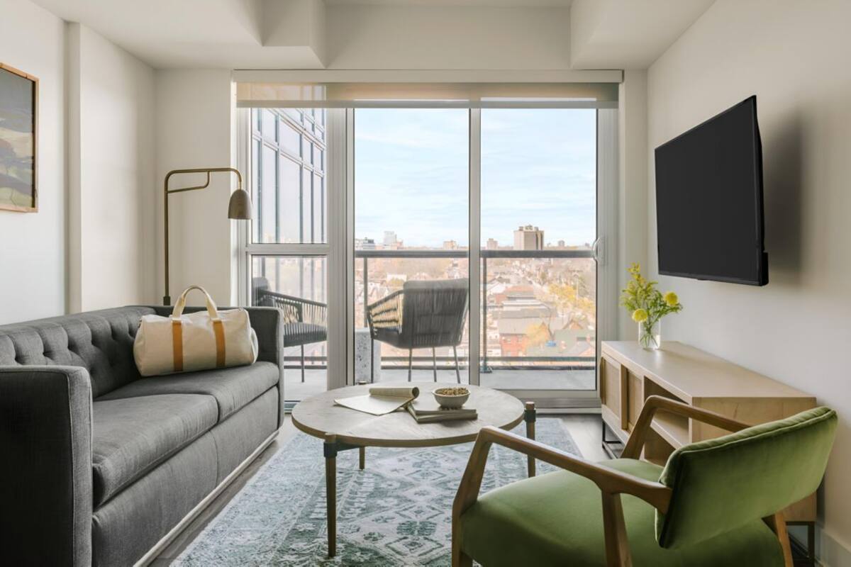 Un salon moderne avec un canapé, un fauteuil vert, une table ronde, un lampadaire et un téléviseur fixé au mur.