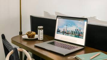 Een laptop op een houten tafel waarop een reisgids voor Toronto, een muffin, een koffiekop en een notitieboek liggen.