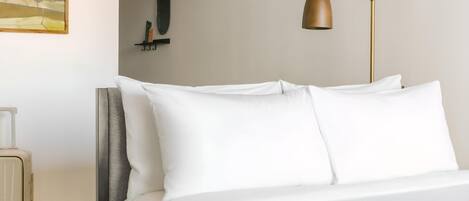 A neatly made bed with white linens, a gold floor lamp, and a painting on the wall.