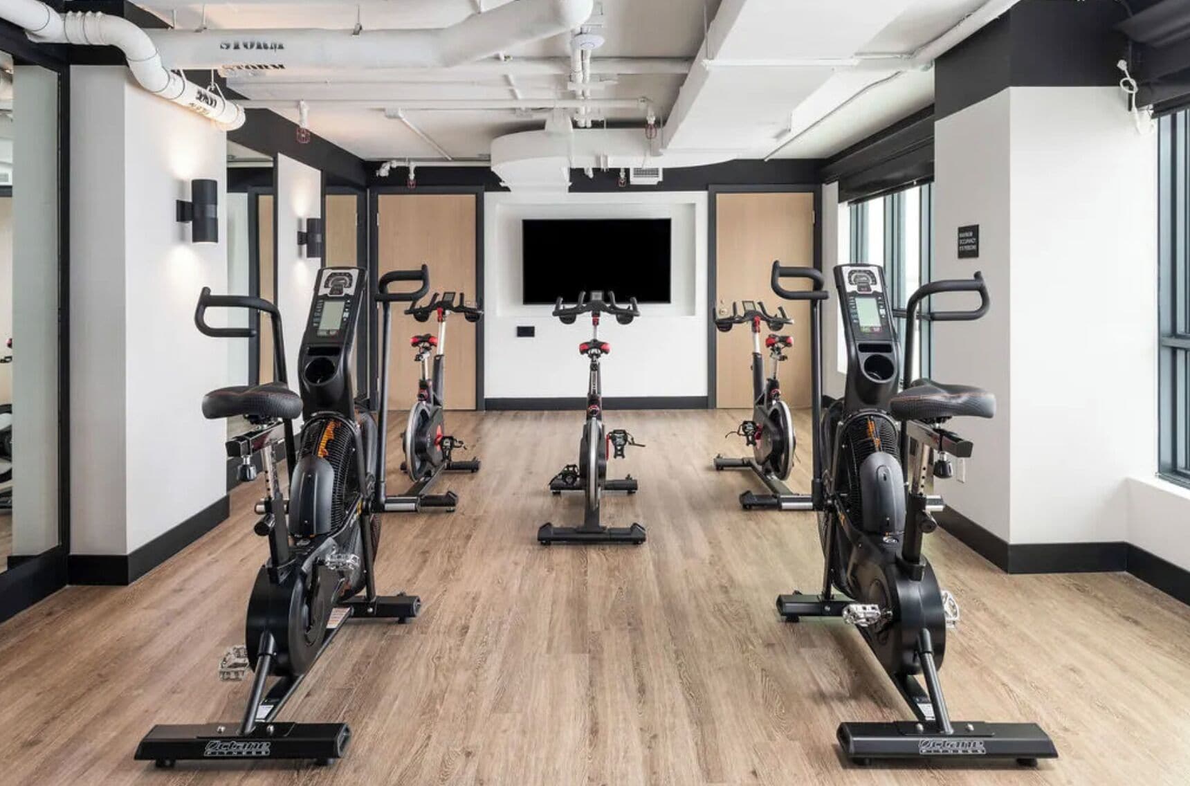 Una palestra con cyclette, uno schermo televisivo e un pavimento in legno.