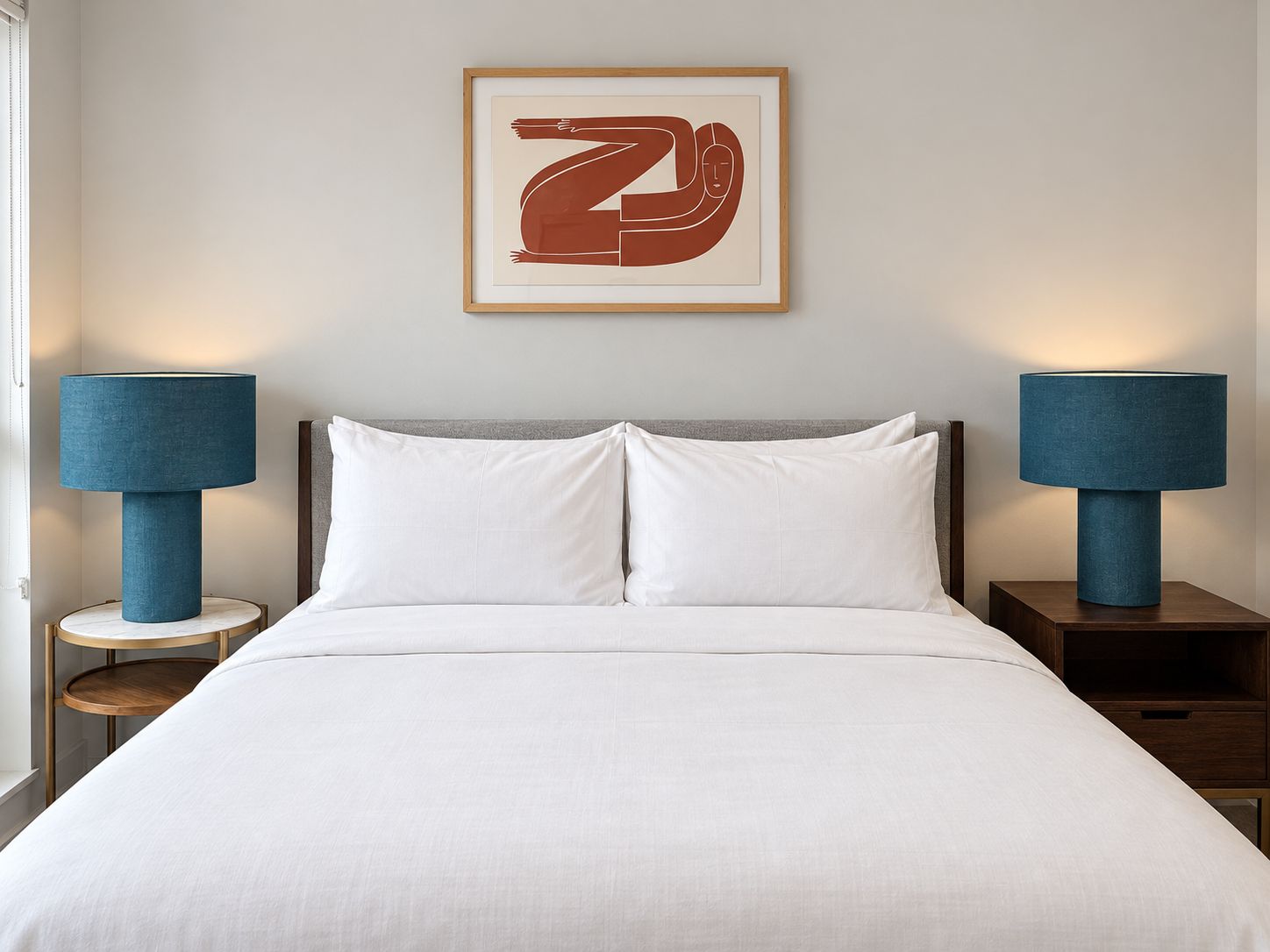 Een net opgemaakt bed met witte lakens, met aan beide zijden nachtkastjes met blauwe lampen, en een ingelijst kunstwerk erboven.
