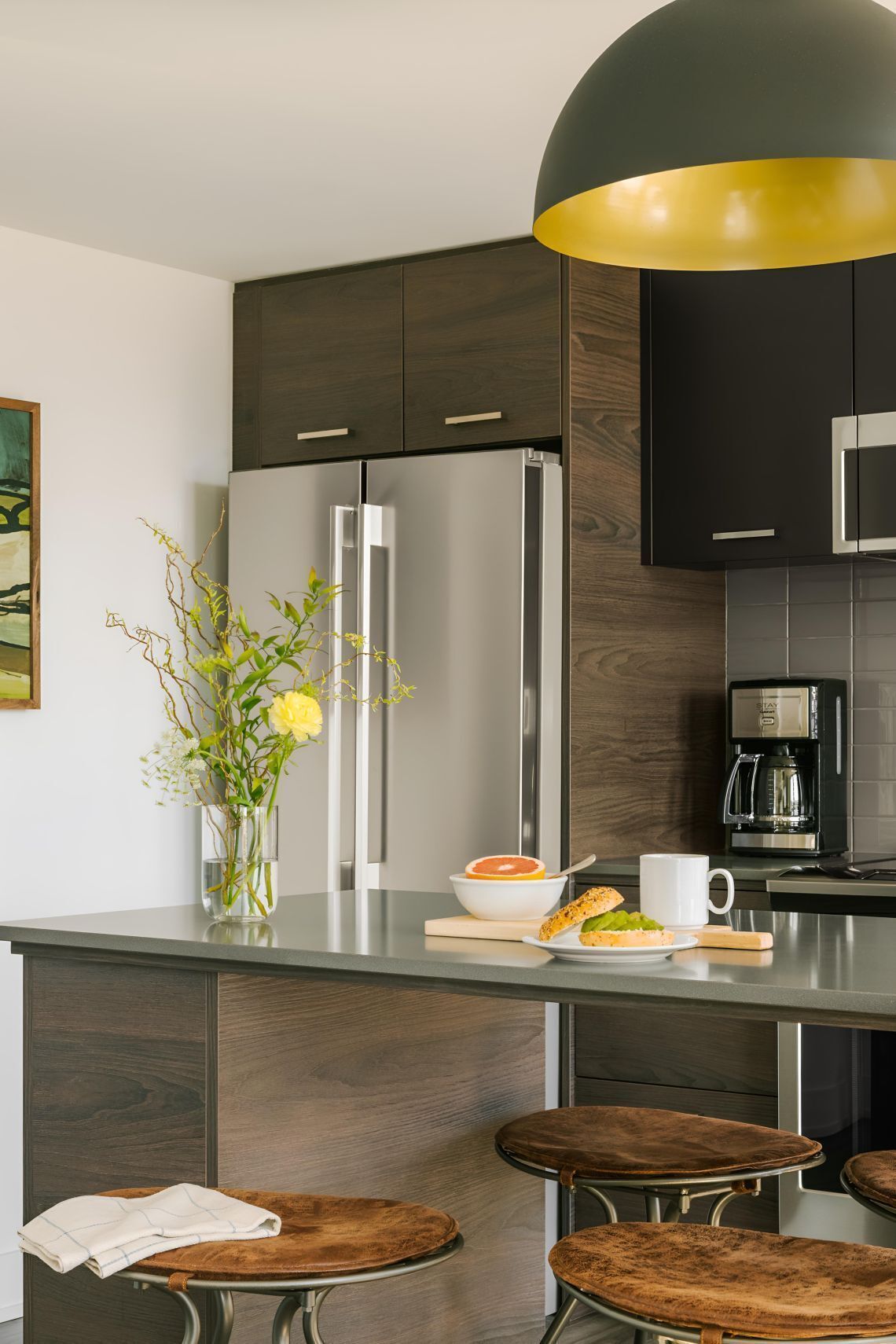 Une cuisine moderne avec des meubles de couleur bois foncé, des appareils électroménagers en acier inoxydable, un îlot central doté de tabourets et un luminaire suspendu.