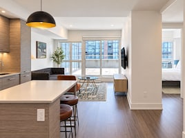 A modern kitchen with a central island, a dining area with a round table, and a living space with a sofa and a TV.