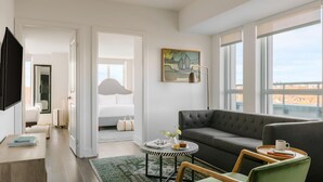 A modern living room with a grey sofa, a round coffee table, and a view of the city through large windows. - Nester Finn West Queen West (Toronto)