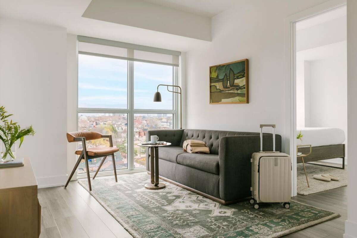 Un salon moderne avec un canapé, une petite table, un fauteuil, une grande fenêtre et un tableau accroché au mur.