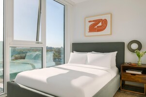 Een moderne slaapkamer met een groot bed, een nachtkastje, een kunstwerk in een lijst en uitzicht op de stad.