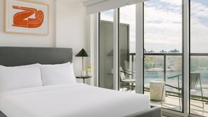 Een moderne hotelkamer met een groot bed, uitzicht op de stad door middel van vloerhoog ramen en een balkon met buitenmeubilair.