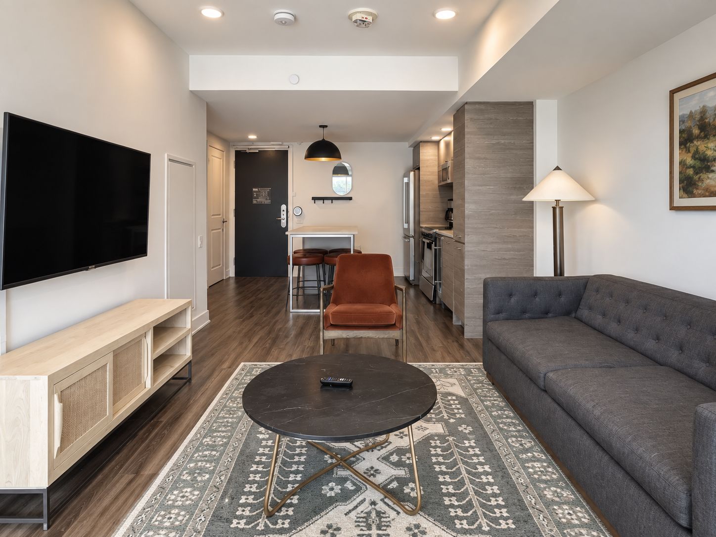 A modern living room with a flat-screen TV, a sofa, a coffee table, and a dining area with a kitchen in the background.