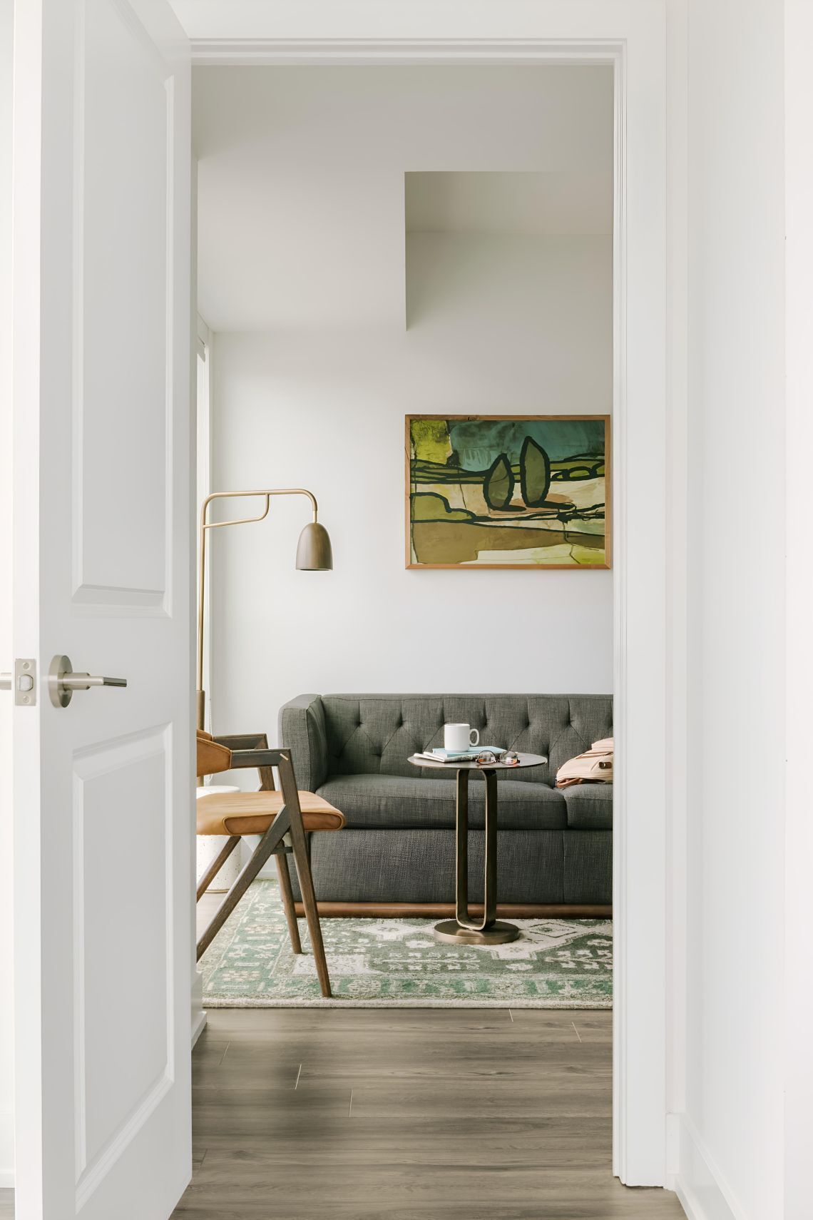 A room with a grey sofa, a small round table, a floor lamp, and a painting on the wall.
