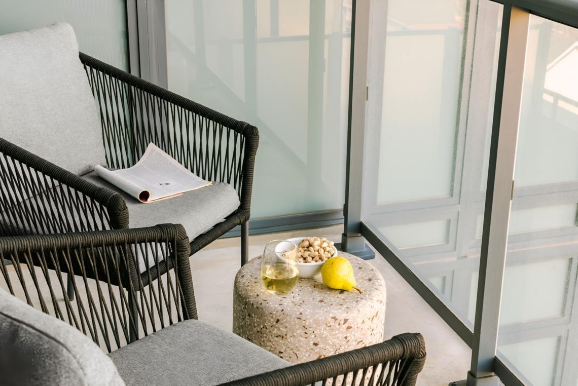 A modern room with a wicker chair, a round ottoman, a bowl of nuts, a glass of wine, and a lemon.