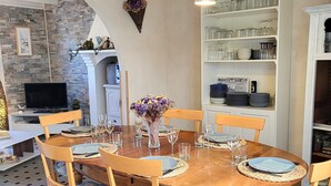 A dining area with a round wooden table, chairs, and a bookshelf with glassware. - Gîte La Rose des Vents: Between Sea and Countryside (Pirou)