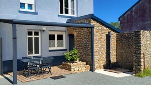 A two-story house with a patio area, stone wall, and a chimney. - Gîte La Rose des Vents: Between Sea and Countryside (Pirou)