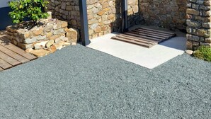A stone wall with a wooden deck, a small garden, and a building with a blue roof. - Gîte La Rose des Vents: Between Sea and Countryside (Pirou)