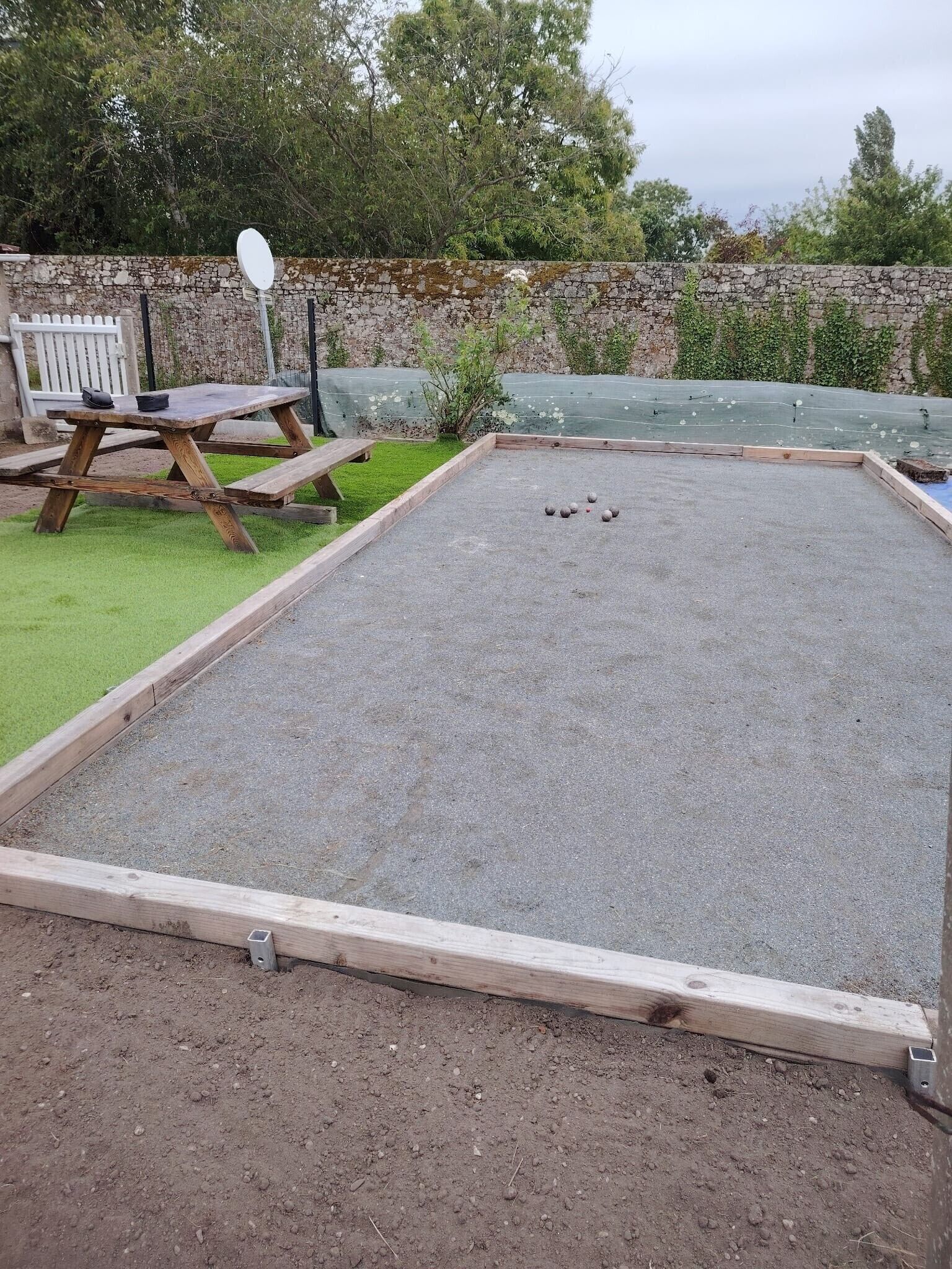 A garden with a wooden table and benches, a paved area with a table tennis table, and a stone wall.