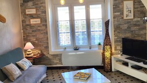 A cozy living room with a sofa, a coffee table, a TV, a fireplace, and a view of the sea through a window. - Gîte La Rose des Vents: Between Sea and Countryside (Pirou)