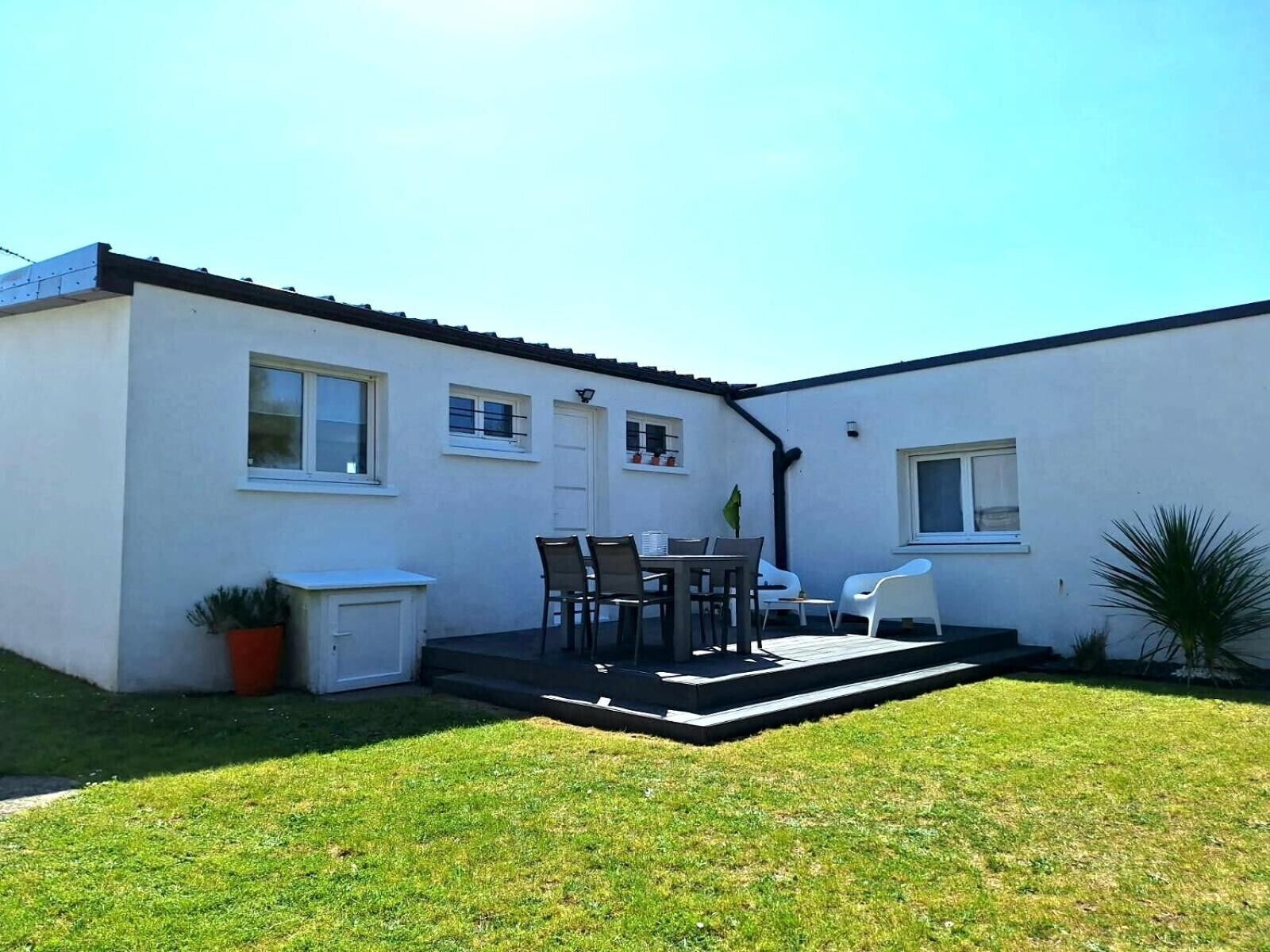 Ein weißes Gebäude mit einer Terrasse, einem Tisch mit Stühlen und einem kleinen Garten.
