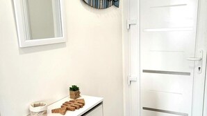 A white cabinet with a mirror above it, a fish-shaped wall decoration, and a white door with a black doormat. - Holiday Home "La Villa Kikifil, Seaside" with Private Terrace, Garden & Wi-Fi (Saint-Germain-sur-Ay)