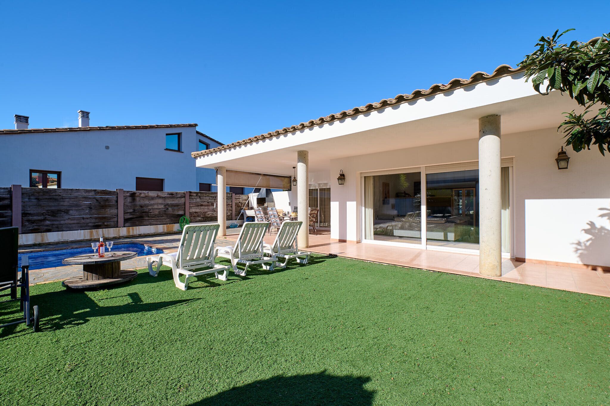 A covered patio with artificial grass, outdoor seating, and a pool.