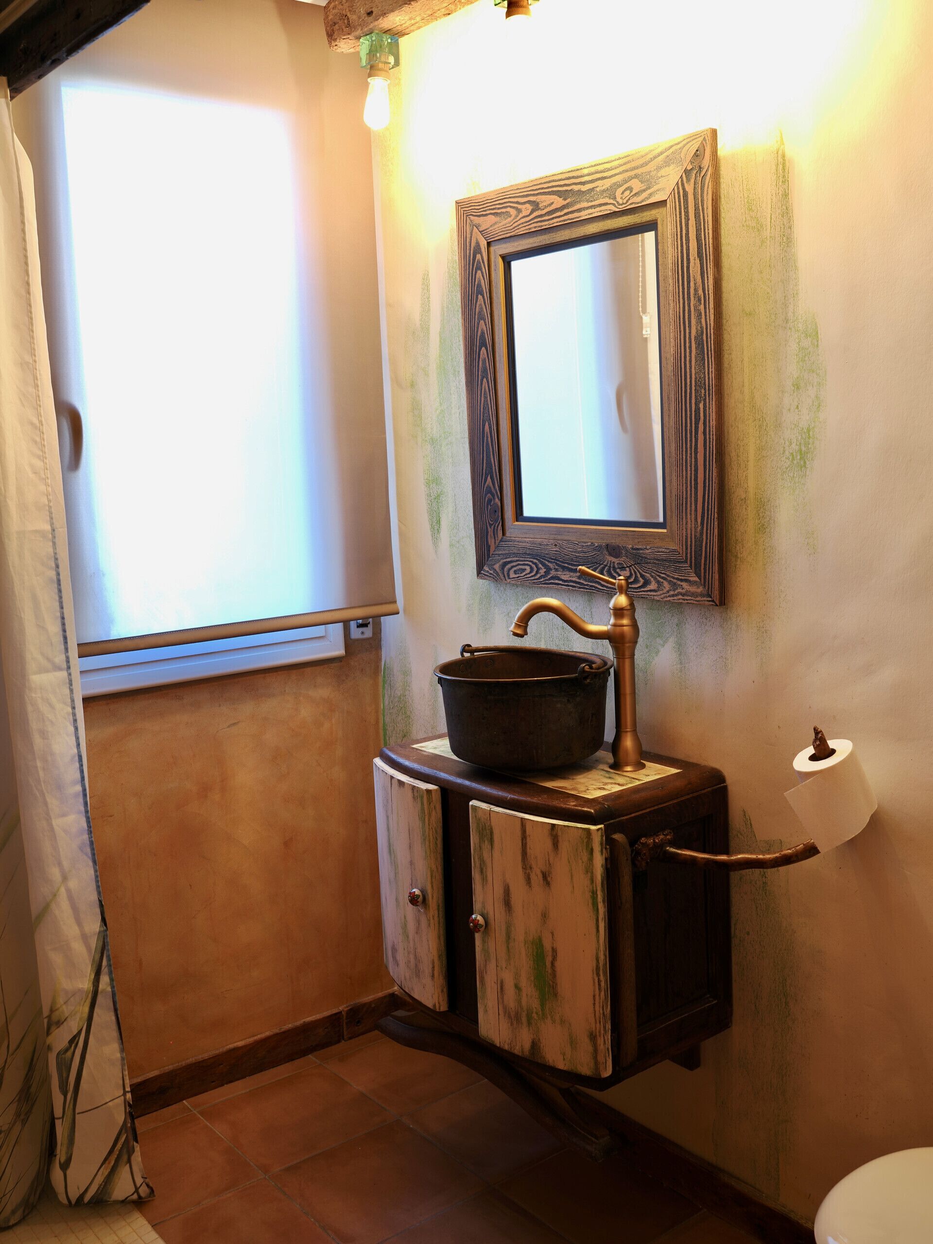 A bathroom with a rustic design, featuring a wooden cabinet, a large mirror, and a vintage-style sink.