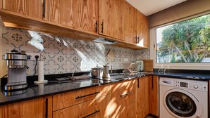 A kitchen with wooden cabinets, a coffee maker, a washing machine, and a window with a view of palm trees. - 1Mel01 - House with private pool for 7 people near one of the most beautiful beaches in Begur (Begur)