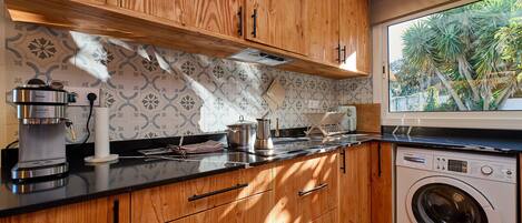 Una cucina con mobili in legno, una macchina da caffè, una lavatrice e una finestra vista palme.