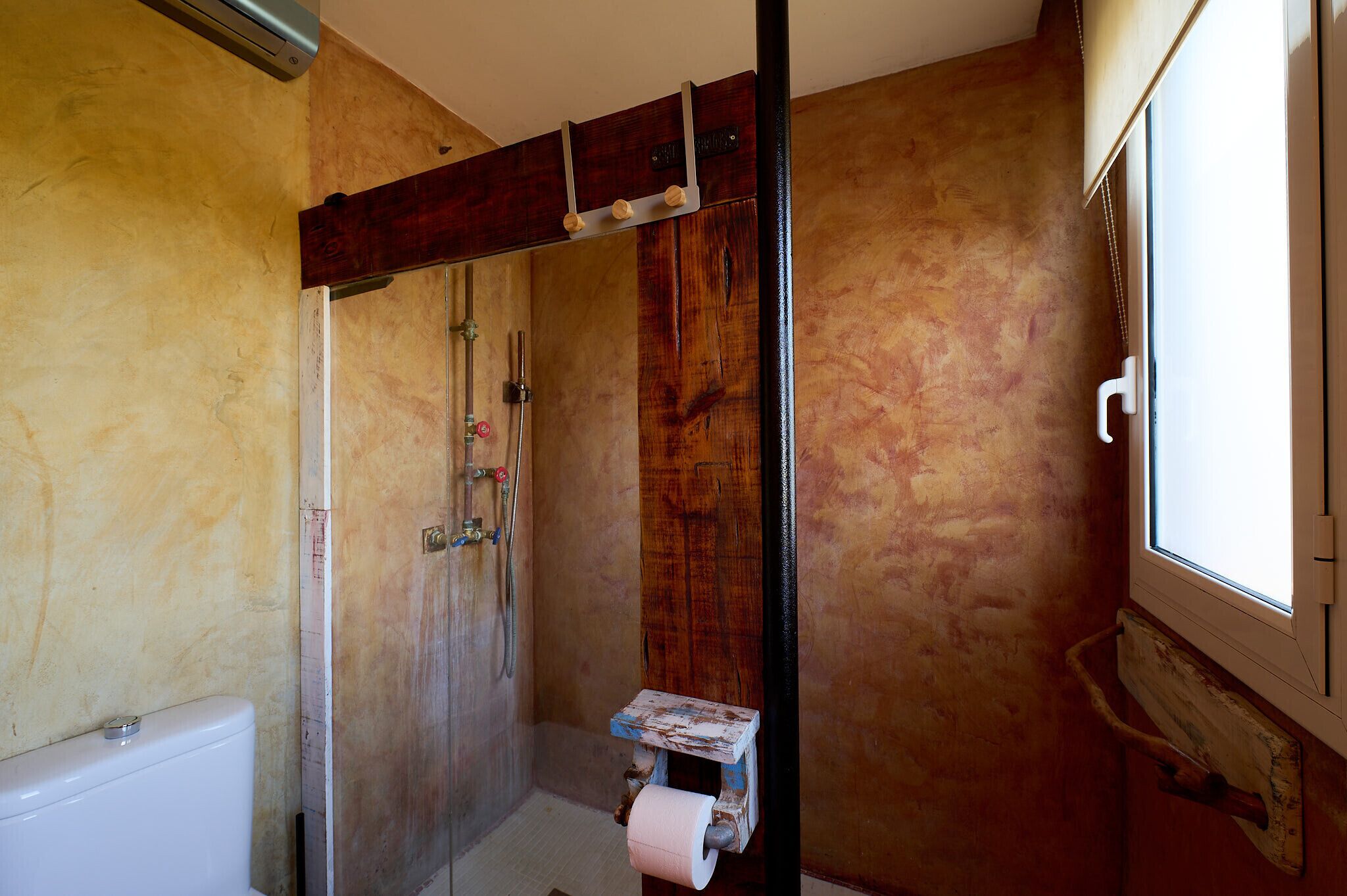 A bathroom with a wooden shower enclosure, a toilet, and a window.