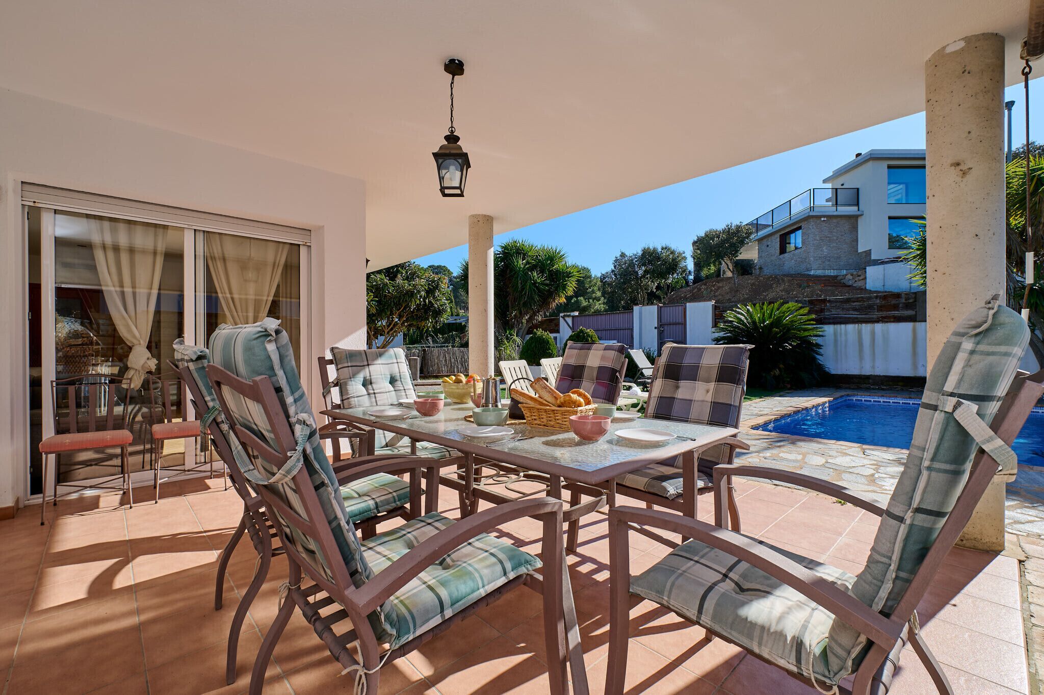 Une terrasse extérieure avec une table dressée pour le repas, entourée de chaises, et une piscine en arrière-plan.