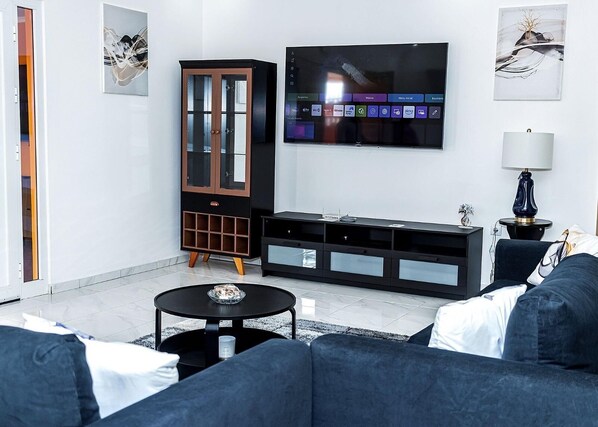 A modern living room with a large flat-screen TV mounted on the wall, a dark wooden cabinet with glass doors, a black entertainment unit, and a blue sofa.