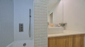 Un baño con bañera, ducha y tocador de madera con lavamanos.