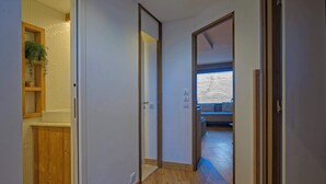 Un pasillo con piso de madera, un armario de madera con una planta y vistas a una habitación con un sofá y una ventana.