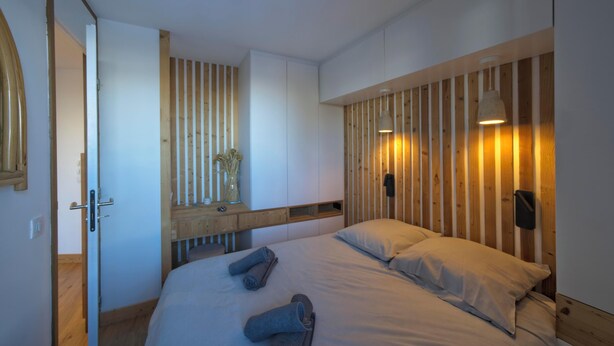 Un dormitorio moderno con un revestimiento de listones de madera, una cama con almohadas, una mesita de noche y un espejo.