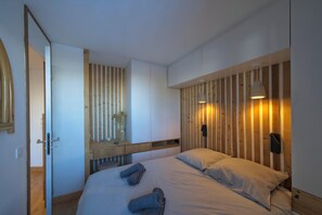 A modern bedroom with a wooden slat wall, a bed with pillows, a bedside table, and a mirror. - Comfortable apartment with mountain view (Les Avanchers-Valmorel)