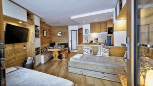 Una habitación compacta y moderna con cama, una pequeña mesa de comedor, kitchenette y televisor.