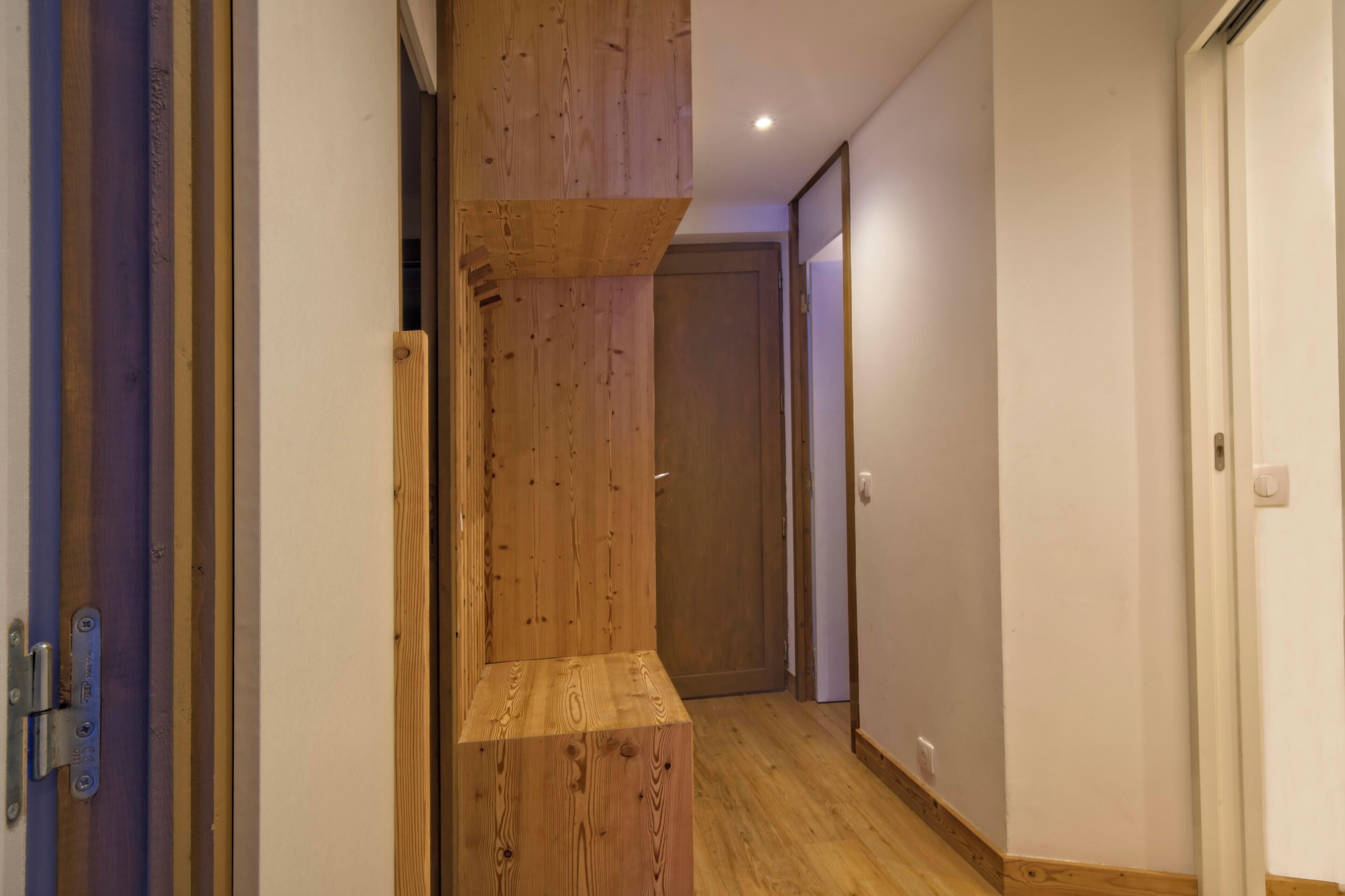 A wooden staircase leading to a door, a hallway with a wooden floor, and a white wall.