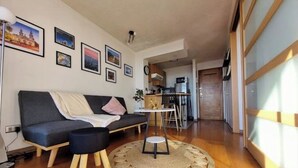 Un salon moderne avec un canapé, une petite table ronde et une cuisine en arrière-plan.