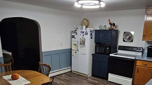A compact kitchen with a dining area, featuring a refrigerator, microwave, stove, and wooden dining table with chairs.