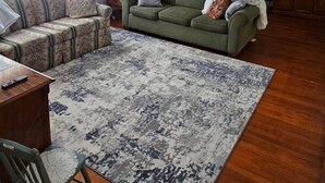 A living room with a sofa, a coffee table, a rug, a wooden floor, and a ceiling fan.