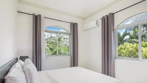 Un dormitorio con cama, cortinas y ventana con vista a follaje.