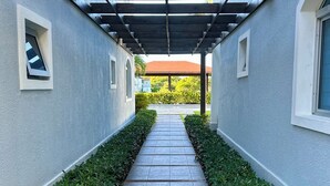 Un paseo techado con baldosas de piedra y setos recortados a ambos lados, que conduce a un edificio con techo rojo.