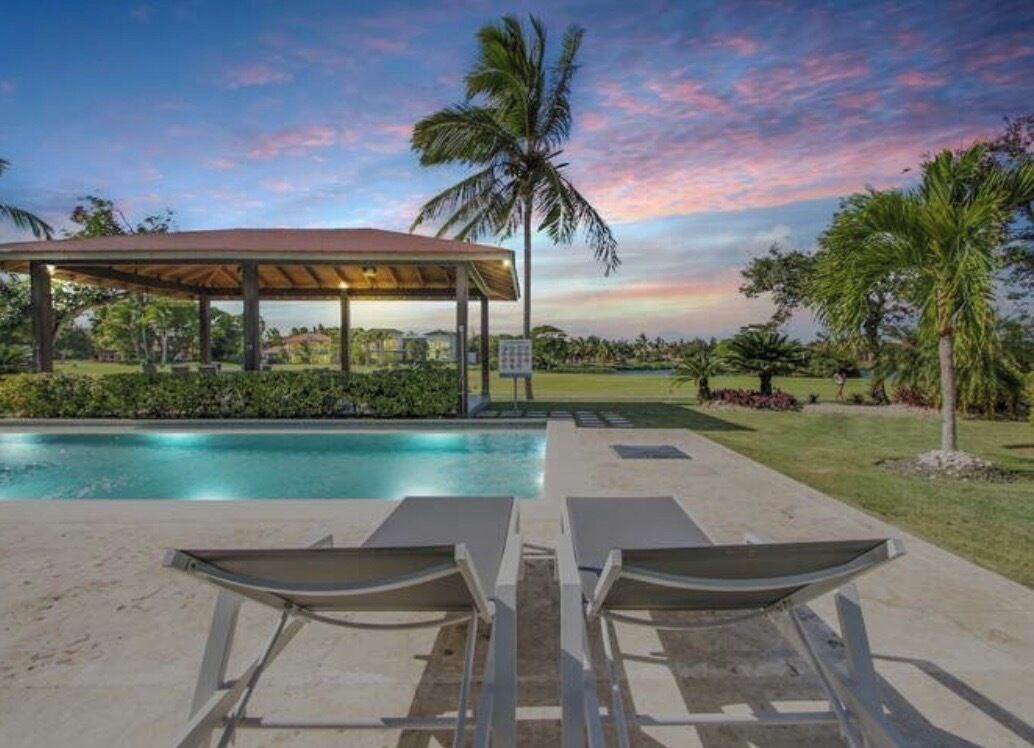 Área à beira da piscina com espreguiçadeiras, um espaço coberto para sentar e vista para a piscina e vegetação ao redor.