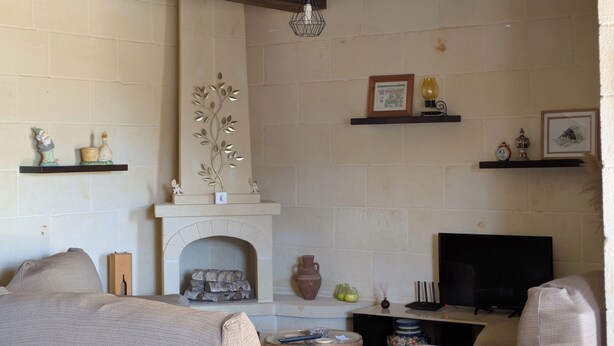Una sala de estar con chimenea, vigas de madera y diversos objetos decorativos en estantes.