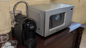 Una cocina con microondas, cafetera y un recipiente de vidrio sobre una encimera de madera.