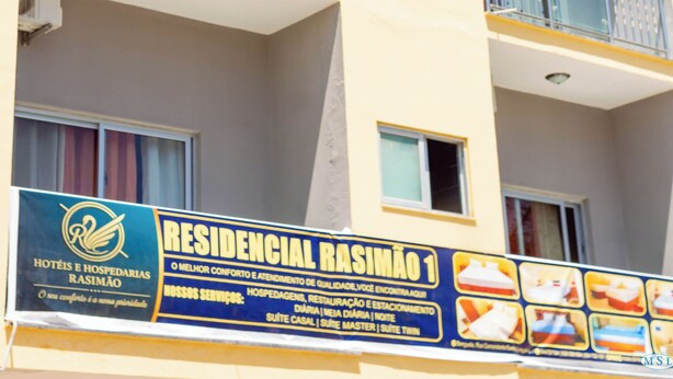 A multi-story building with balconies, a sign advertising a hotel, and a clear blue sky. - Hospedaria RaSimão 1 (Benguela)