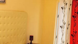 A bedroom with two single beds, a bedside table with a lamp, a curtain, and a framed picture on the wall. - Hospedaria RaSimão 1 (Benguela)