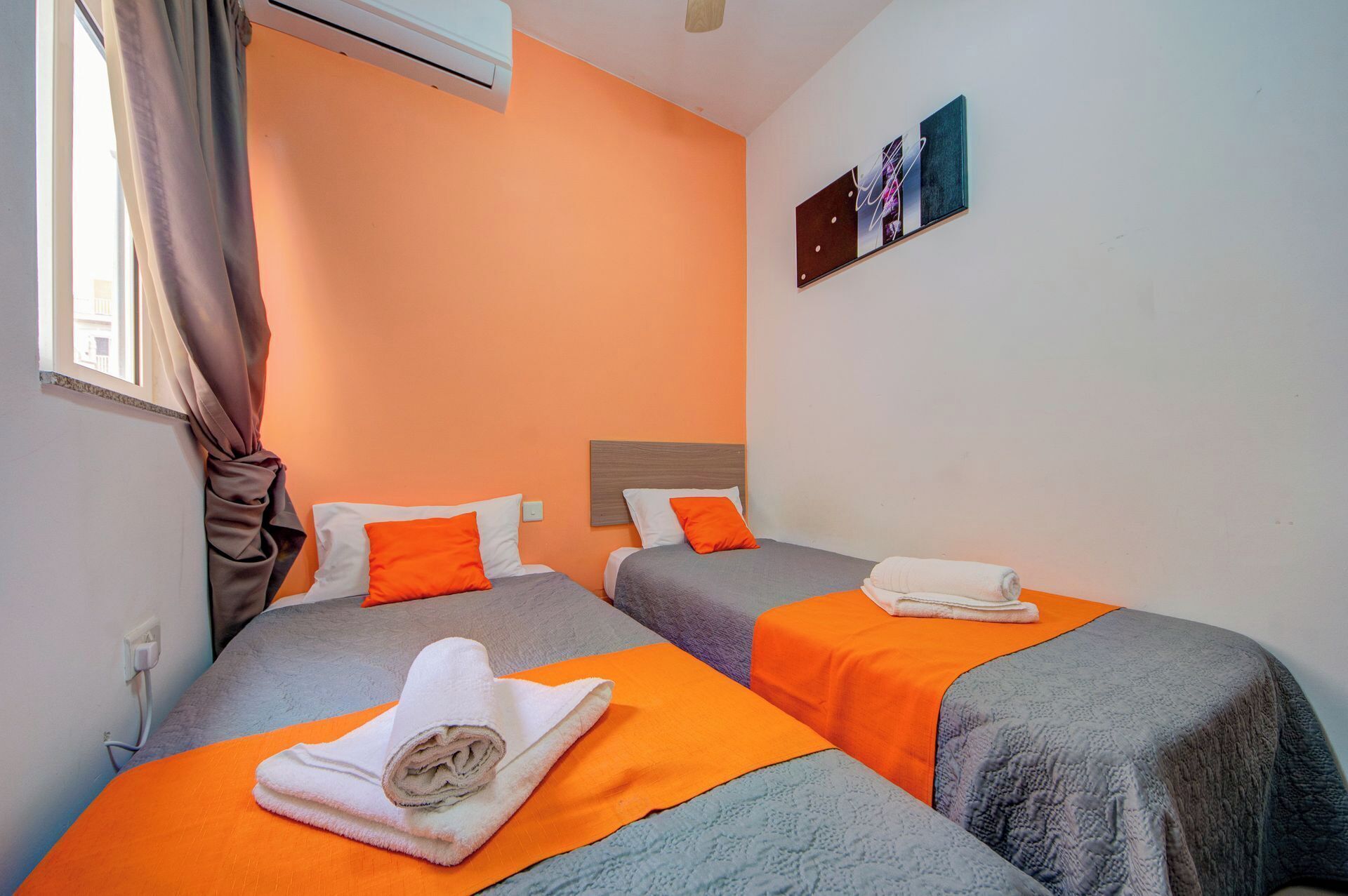 A room with two beds, orange bedding, and a wall art piece.