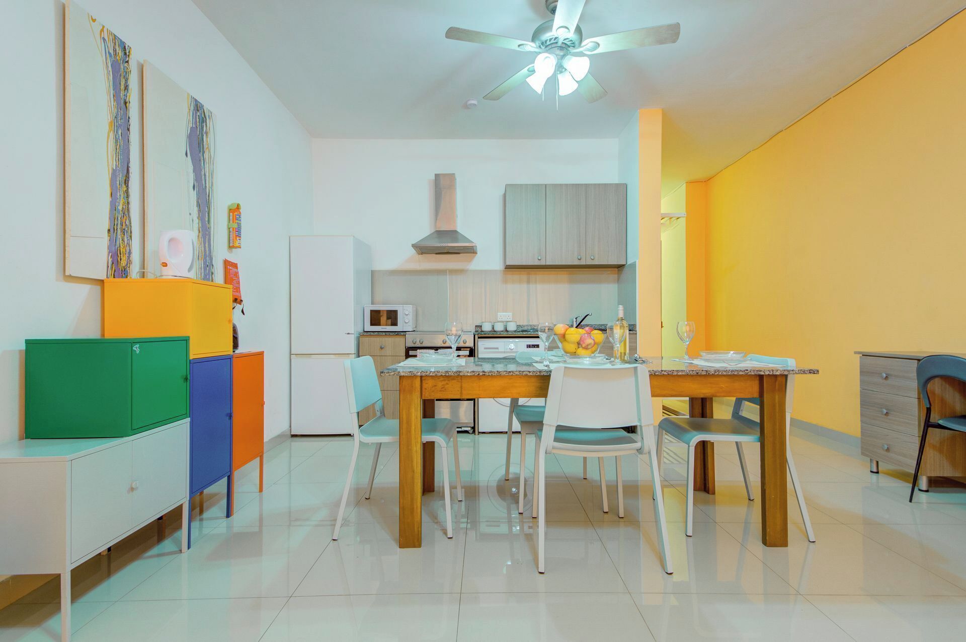 A modern kitchen with a dining area, featuring a white ceiling fan, a microwave, and a dining table set for four.
