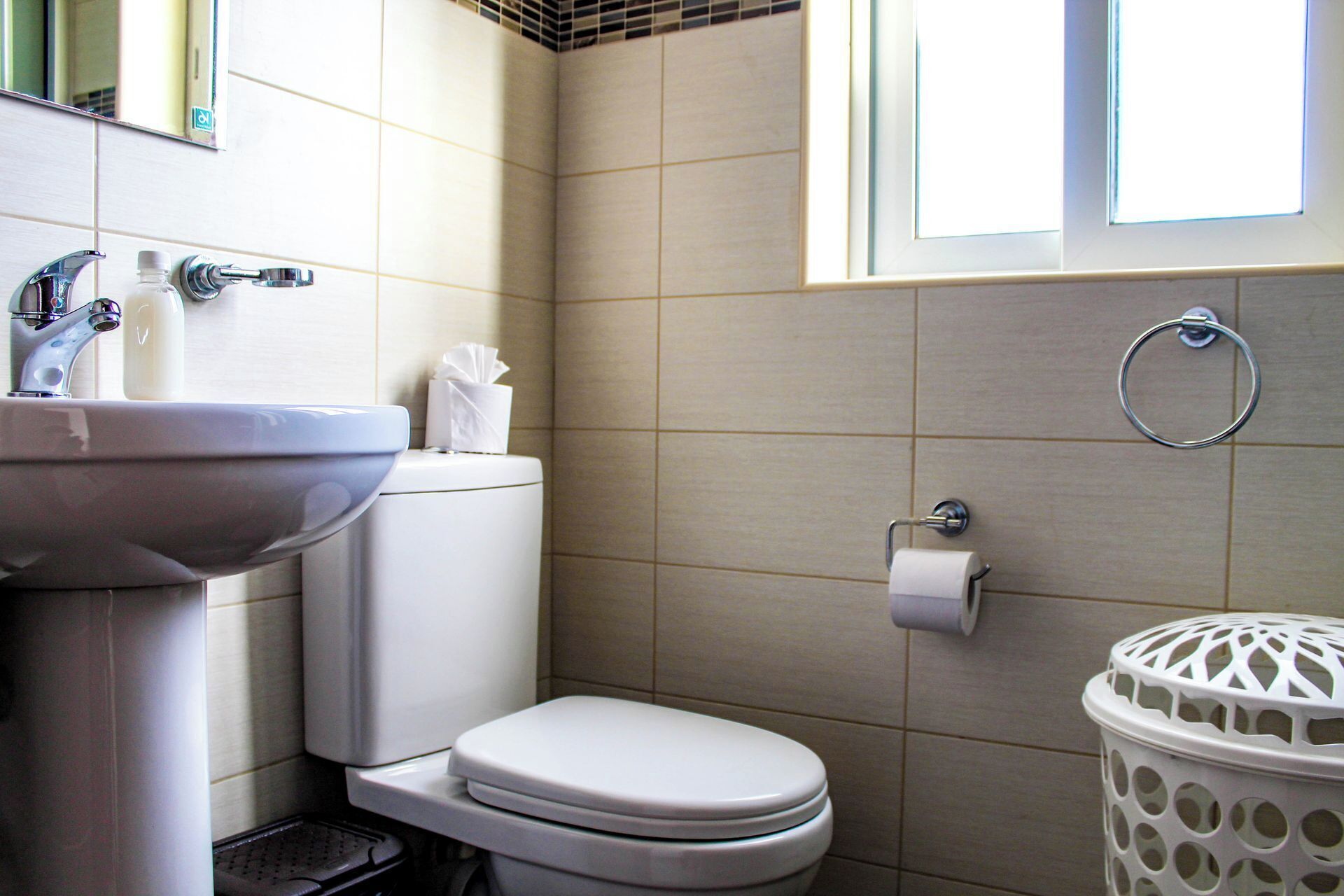 Une salle de bain avec un lavabo blanc, des toilettes et une fenêtre située au-dessus des toilettes.