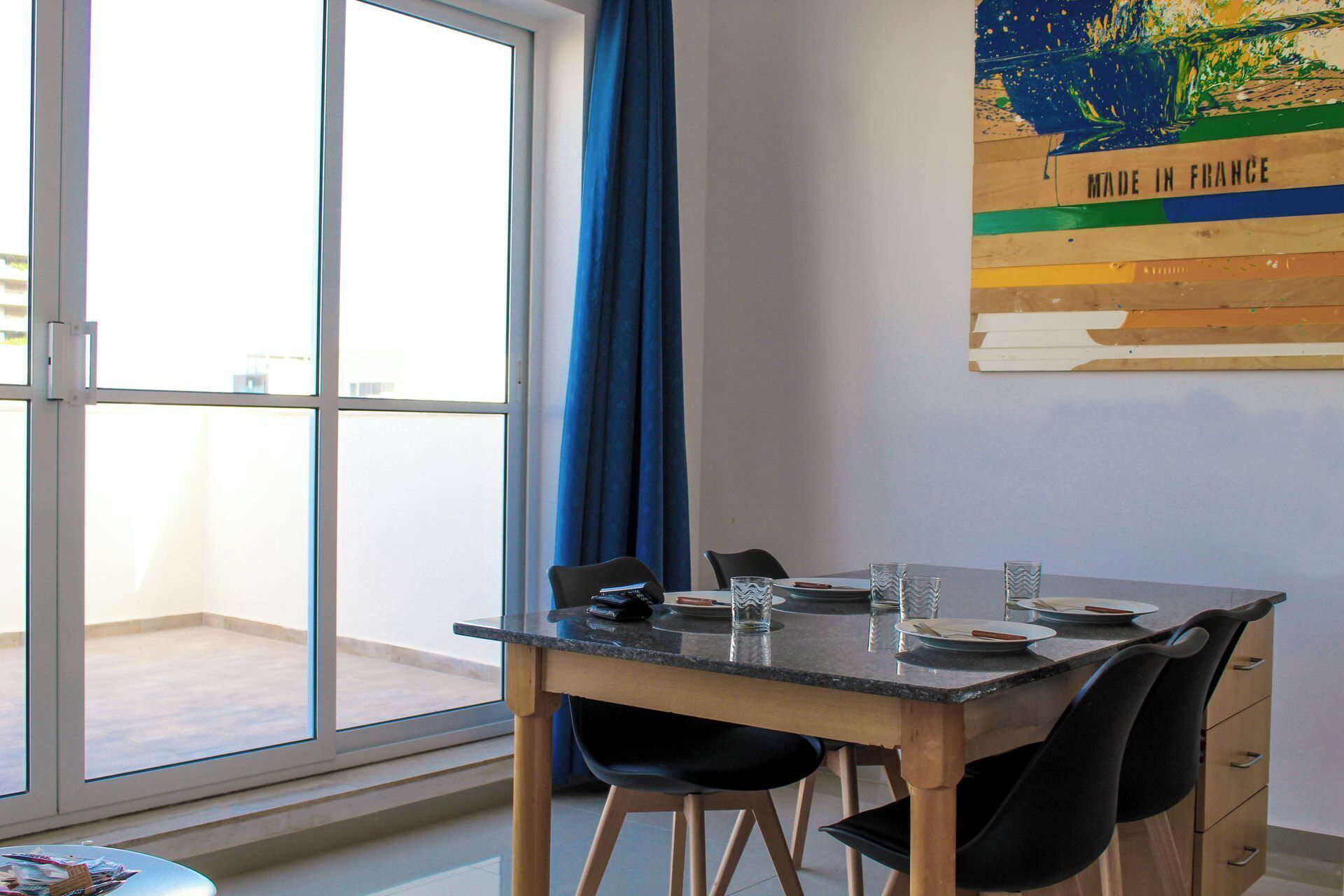 A dining area with a table set for four, a window with a view, and a 'Made in France' sign on the wall.